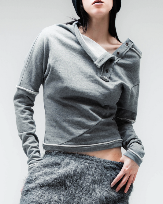 A model wearing a gray long-sleeve cropped henley top, fuzzy gray pants, and a dark navy beanie, photographed against a light gray studio background.